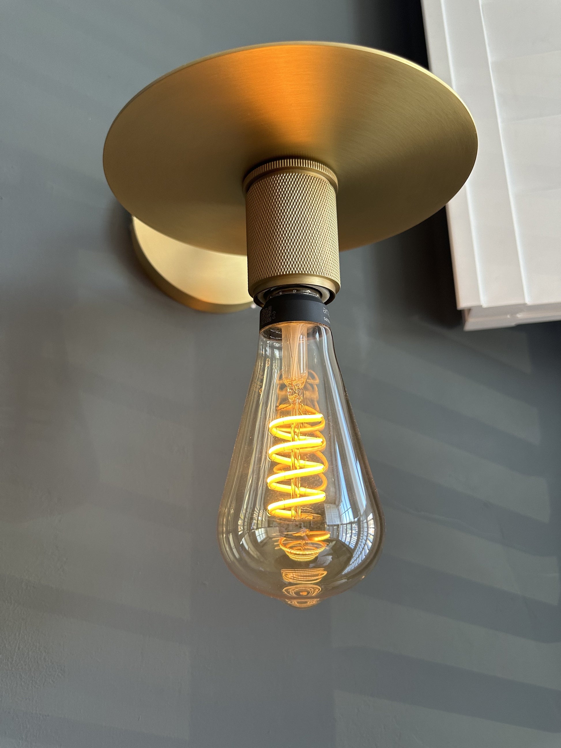 Brass wall light with a filament bulb and disc on a black background