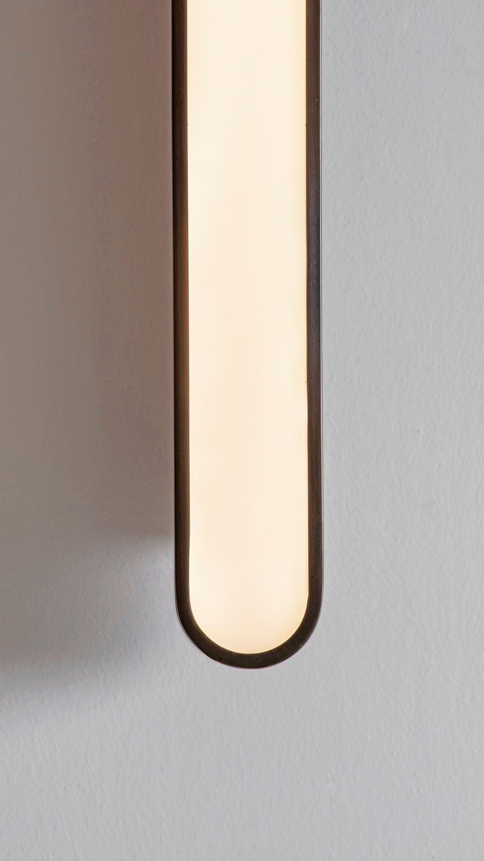 Capsule Wall Light dark bronze, detailed close up view of finish, light on.